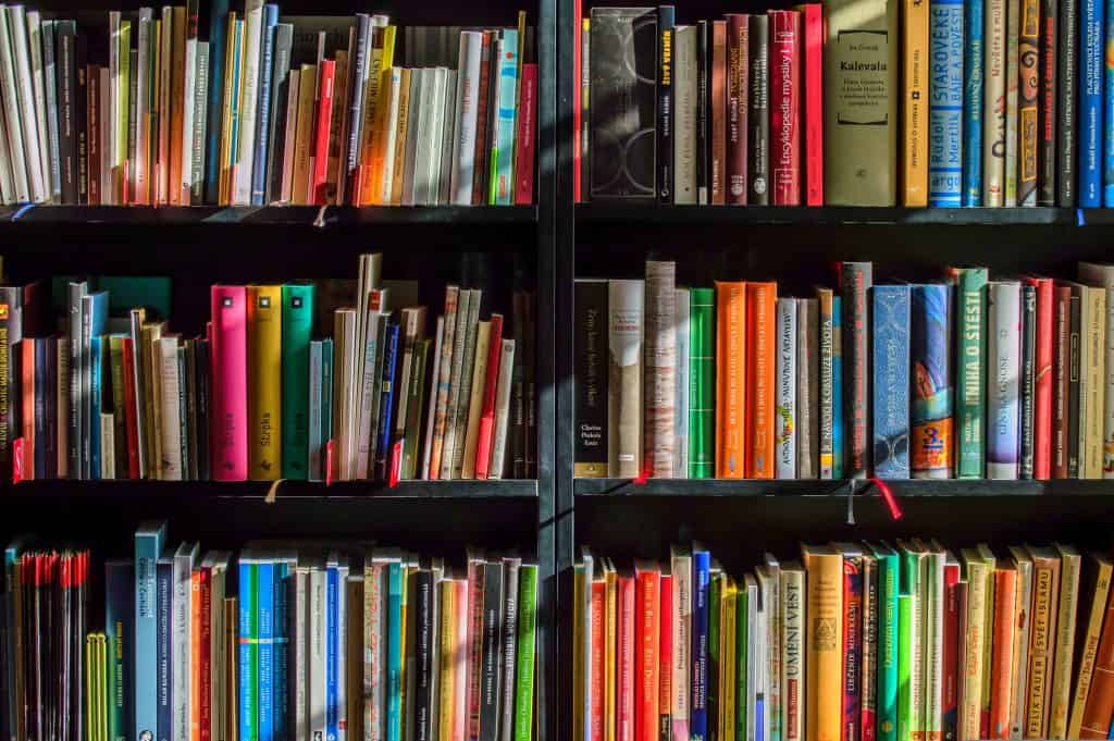 A bookshelf full of brightly coloured books. There are two black bookshelves butted up to each other with two shelves each